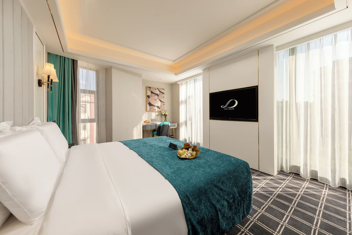 A hotel room with a large bed, a desk with a chair, a television, and a window with curtains.