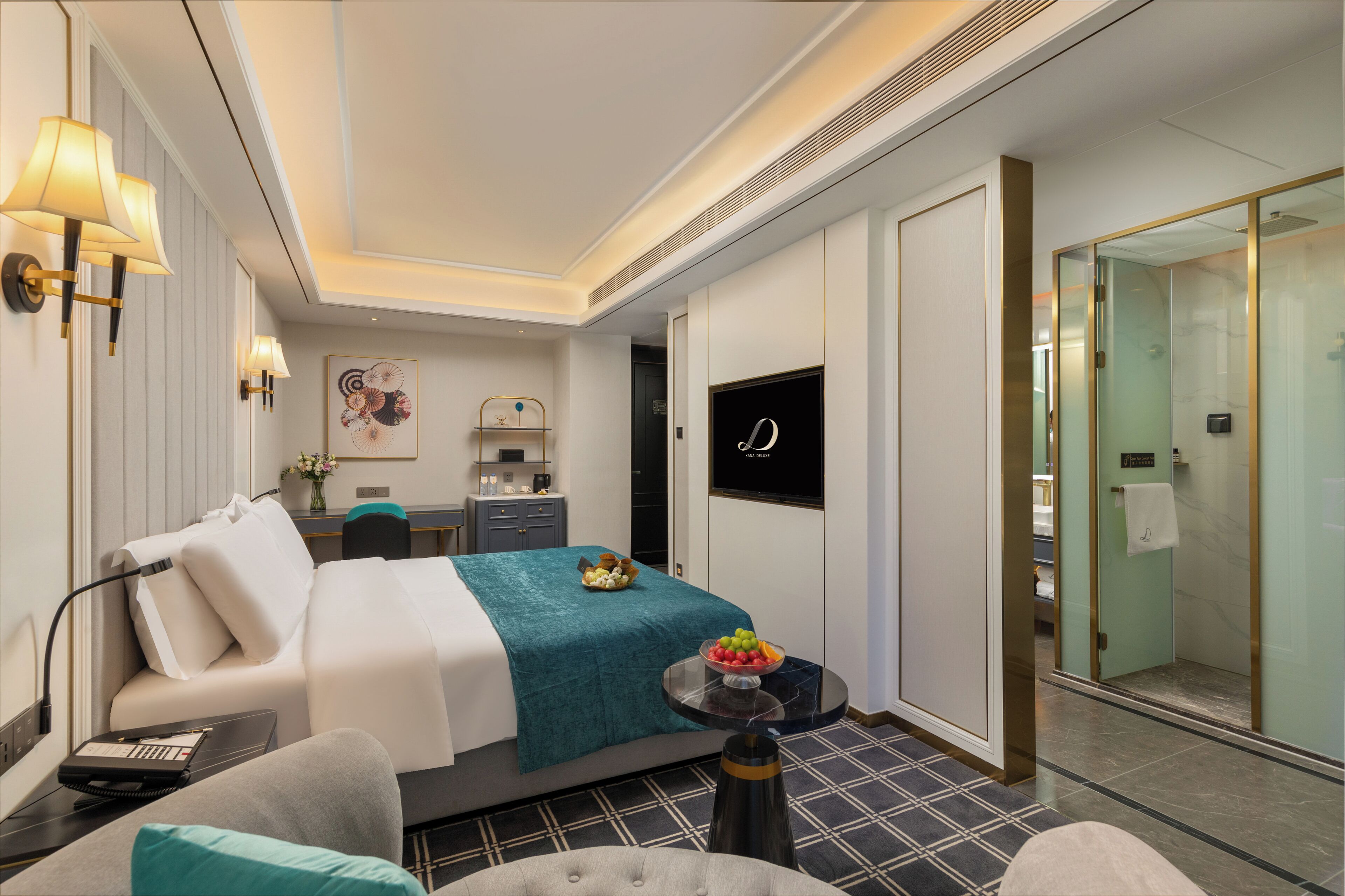 Una habitación de hotel moderna con cama, mesita de noche, lámpara y una pequeña mesa redonda con fruta.