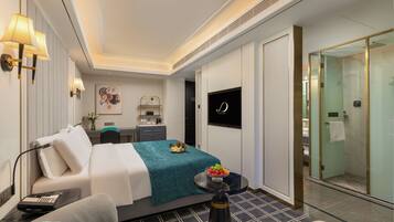 Una habitación de hotel moderna con cama, mesita de noche, lámpara y una pequeña mesa redonda con fruta.