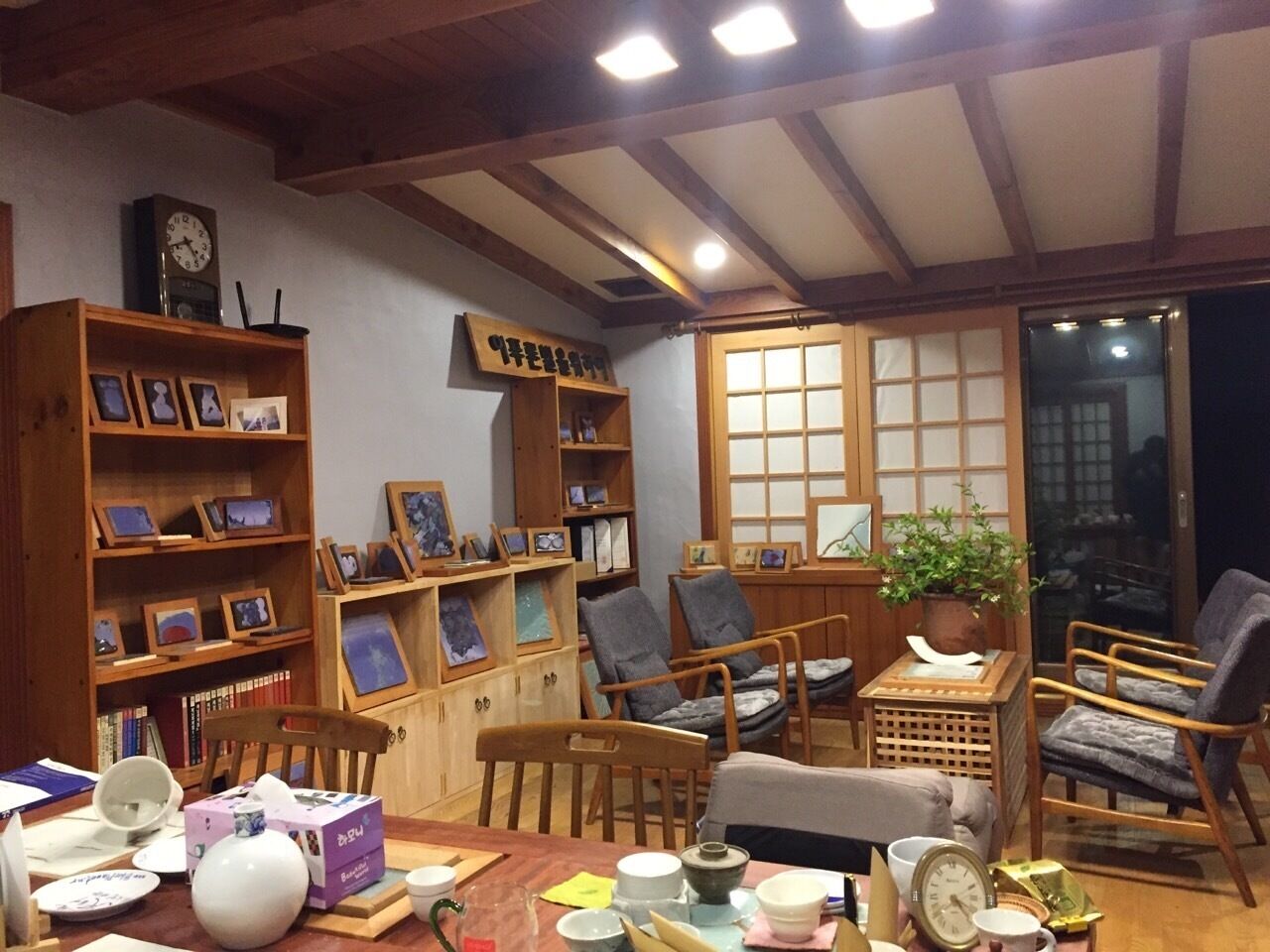Une pièce chaleureuse, meublée de meubles en bois, avec une bibliothèque, une table sur laquelle sont posés des tasses et un vase, et une fenêtre donnant sur un beau paysage.