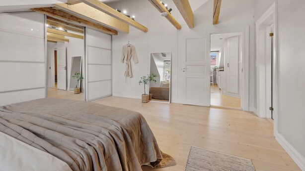 Une chambre avec un grand lit, des poutres en bois, un miroir et une vue sur une autre pièce.