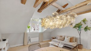 Un loft moderne avec des poutres apparentes, un coin repas doté d’une table ronde et un espace de vie chaleureux avec un canapé et une plante en pot.