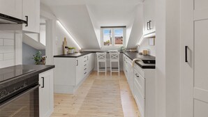 Une cuisine moderne avec des meubles blancs, un plan de travail noir et un plancher en bois. Une fenêtre offre une vue sur un bâtiment à l’extérieur.
