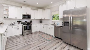A modern kitchen with white cabinets, stainless steel appliances, and a wooden floor.