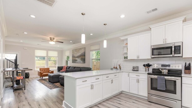 A modern kitchen with white cabinetry, a central island, stainless steel appliances, and a dining area with a sofa and table.