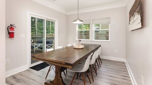 A dining area with a wooden table, white chairs, a pendant light, and a fire extinguisher.