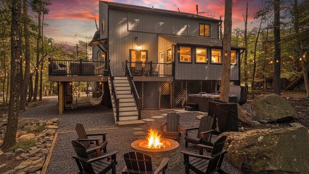 Una cabaña moderna de dos pisos con terraza, asientos exteriores y un pozo de fuego.