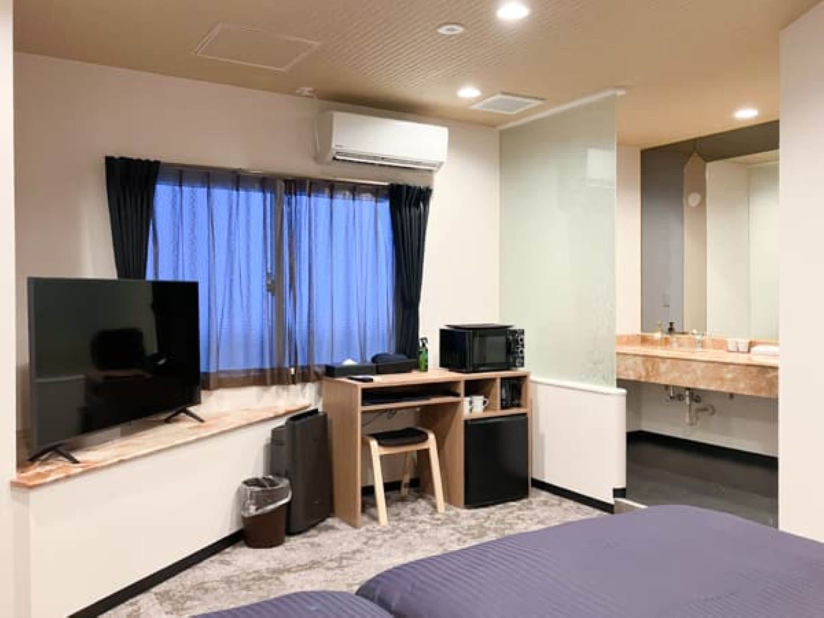 A hotel room with a bed, a TV, a desk with a computer, a microwave, and a small fridge.