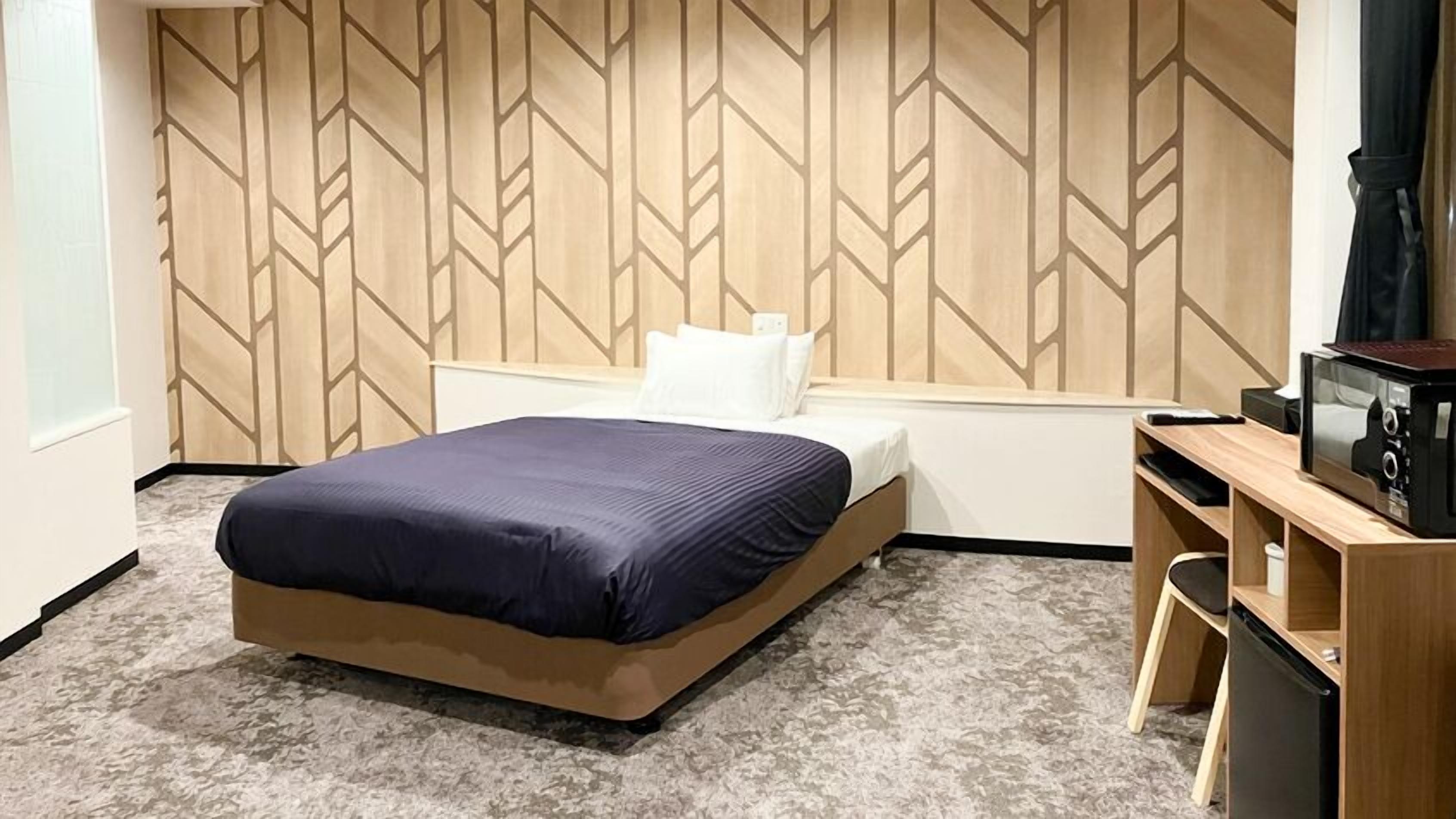 Une chambre d’hôtel avec un lit, un bureau doté d’un micro-ondes et un mur orné d’un motif géométrique.