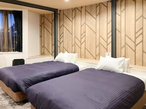 Une chambre d’hôtel avec deux lits, une fenêtre avec des rideaux, un panneau mural en bois et une petite table.