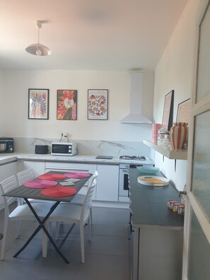Una cucina moderna con tavolo da pranzo, pensili bianchi, microonde, piano cottura a gas ed elettrodomestici inclusa la lavastoviglie.