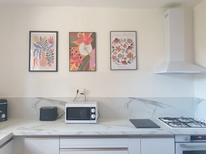 A kitchen with a microwave, toaster, and gas stove. There are three framed artworks on the wall.