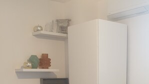 A compact kitchen with a table and chairs, a refrigerator, and shelves with various items. - Seasonal rental apartment between pool and sea. (Arles)