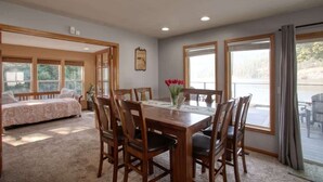 A room with a wooden dining table, chairs, a bed, and large windows. - Lakefront Retreat w/ Private Dock & Fire Pit (Rathdrum)