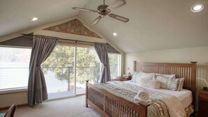A bedroom with a sloped ceiling, a bed with a wooden headboard, a nightstand, and a window with curtains. - Lakefront Retreat w/ Private Dock & Fire Pit (Rathdrum)