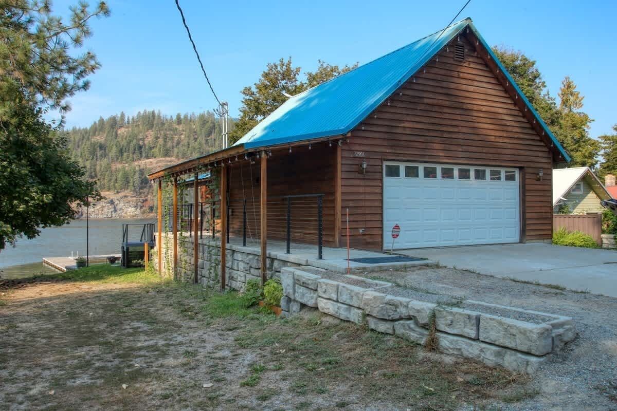 Une cabane en bois avec un toit bleu, une véranda et un garage.