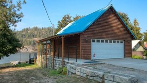 A wooden cabin with a blue roof, a covered porch, and a garage. - Lakefront Retreat w/ Private Dock & Fire Pit (Rathdrum)