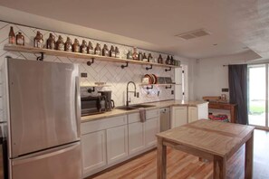 A modern kitchen with a stainless steel refrigerator, wooden shelves above the counter, and a wooden dining table.