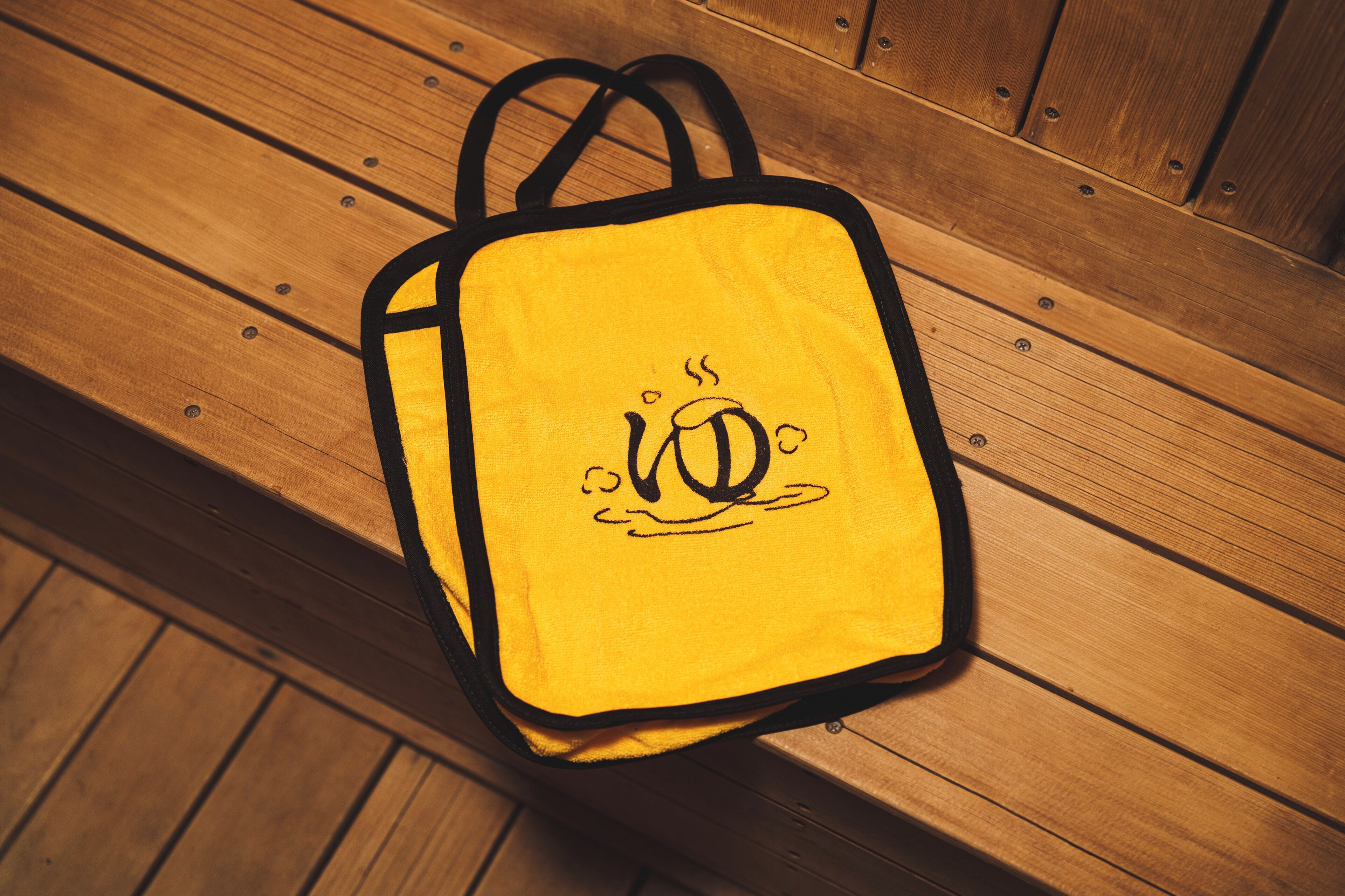 A yellow bag with a black handle and a black design on it, placed on a wooden bench.