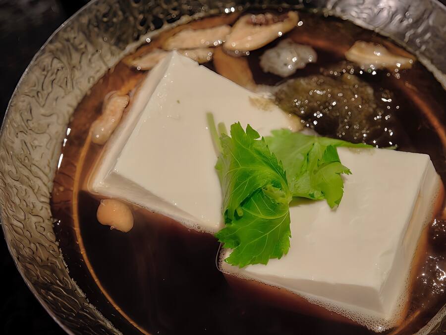 Un bol de soupe contenant du tofu, des champignons et garni de feuilles vertes.