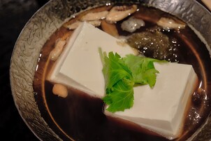 Una ciotola di zuppa con tofu, funghi e un guarnizione di foglie verdi.
