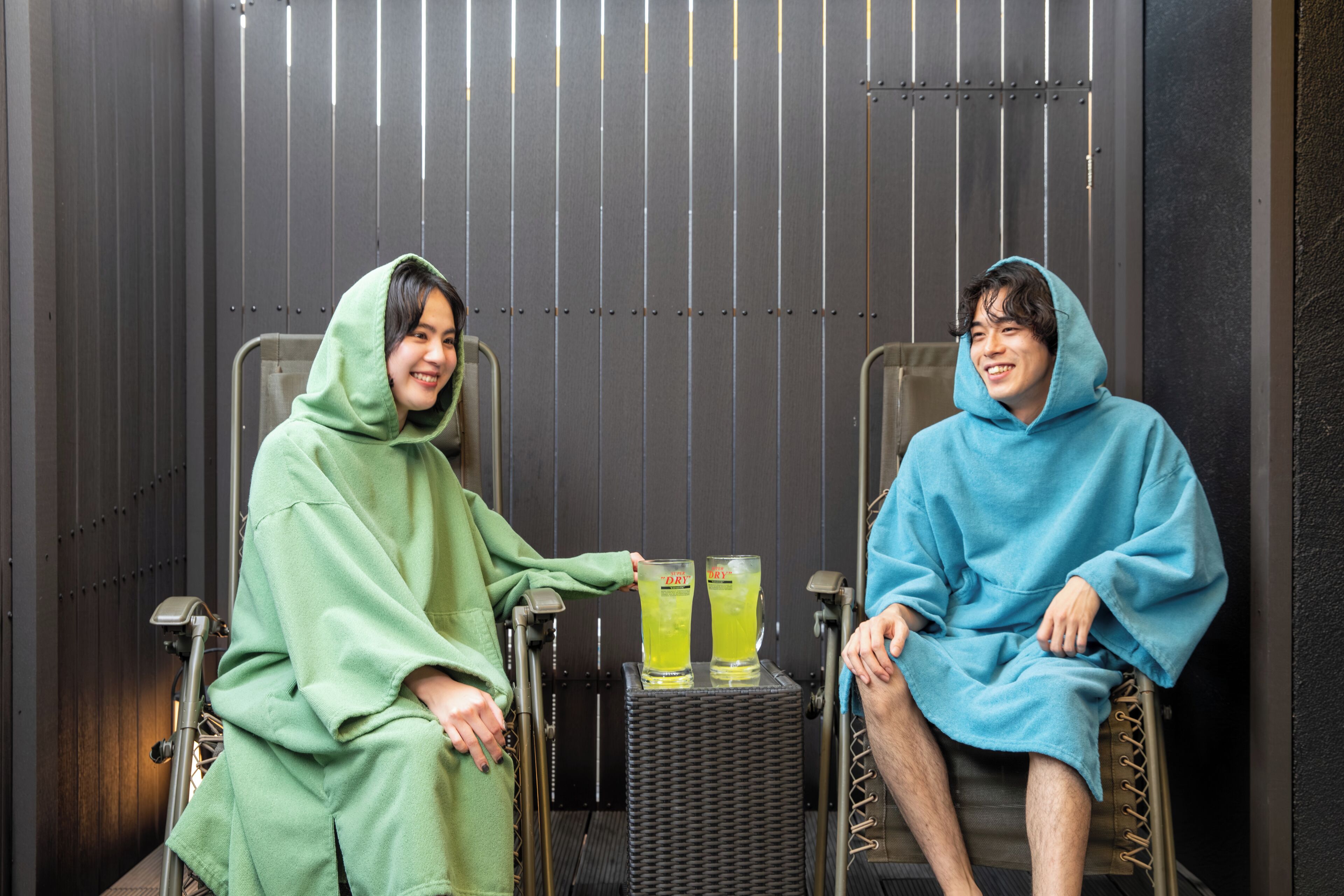 Dos personas en una habitación con sillas metálicas y una pequeña mesa con bebidas.