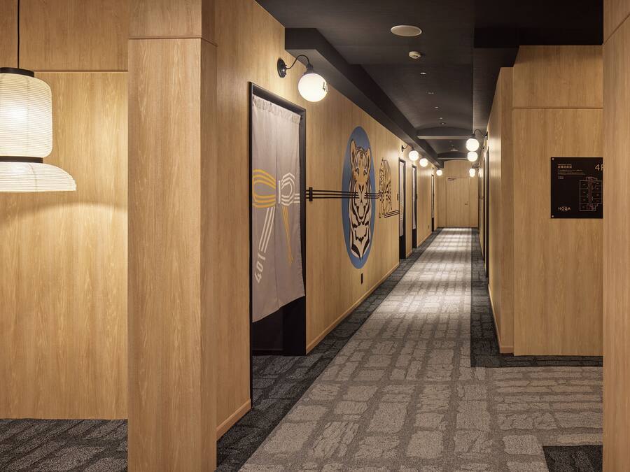 Ein Hotelgang mit Holzwänden, einem gemusterten Teppich und mehreren Türen, die jeweils ein Tigerlogo zeigen.