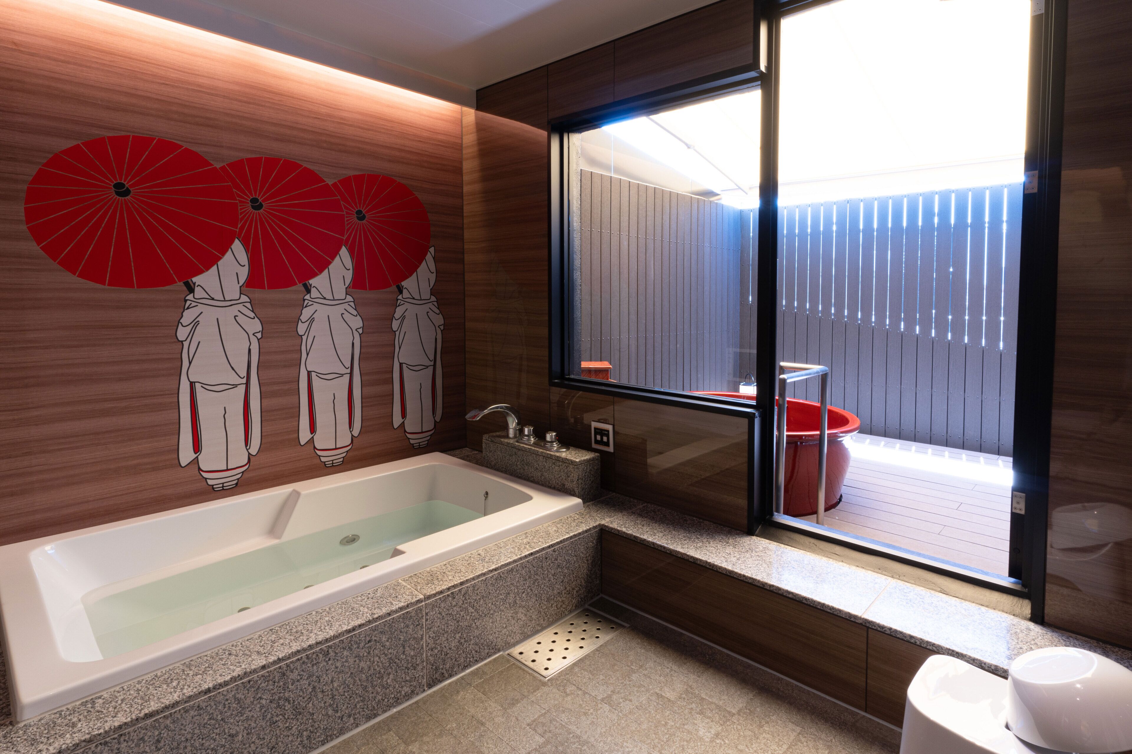 A modern bathroom with a bathtub, a window with a view of a wooden deck, and decorative red umbrellas on the wall.