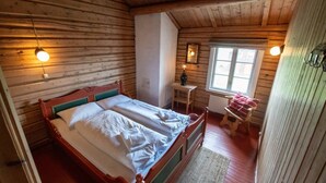 A wooden cabin bedroom with a bed, a small table, a chair, and a window. - Skotten Seter Bed Husky (Ringebu)