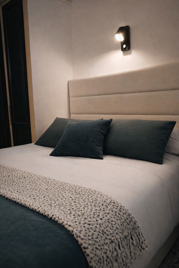 A bed with a headboard, two pillows, a blanket, and a wall-mounted light fixture.