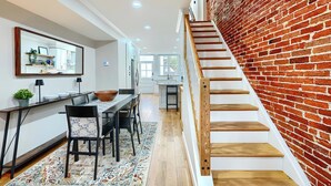 A modern kitchen with white cabinets, a wooden dining table, and a large mirror above it. - Bright & Beautiful 4BR Home + Parking, Walk to Harbor & Stadiums (Baltimore)