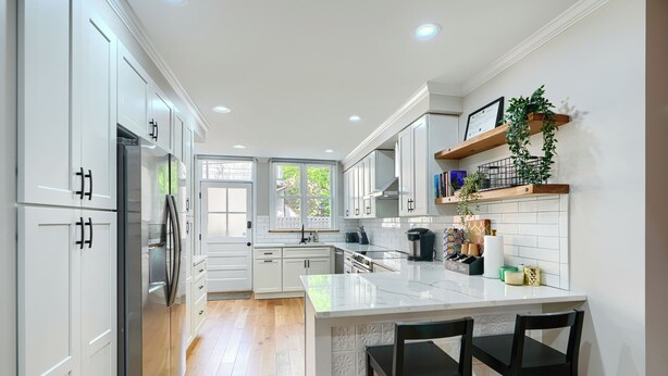 A modern kitchen with white cabinets, a central island with bar stools, and a view to the outside. - Bright & Beautiful 4BR Home + Parking, Walk to Harbor & Stadiums (Baltimore)