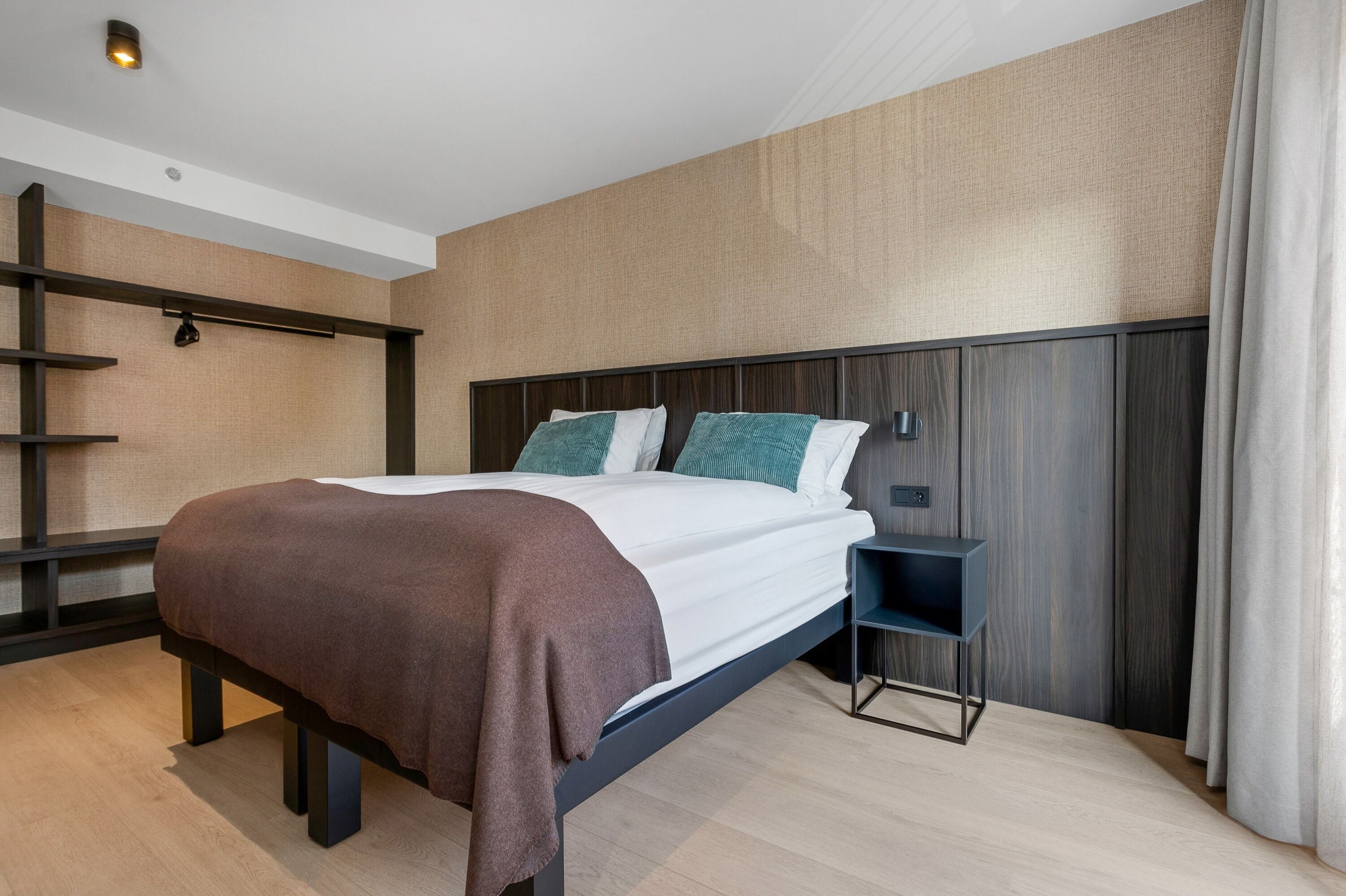 A modern hotel room with a large bed, a bedside table, and a built-in shelf.