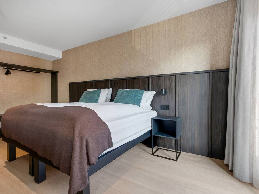A modern hotel room with a large bed, a bedside table, and a built-in shelf.