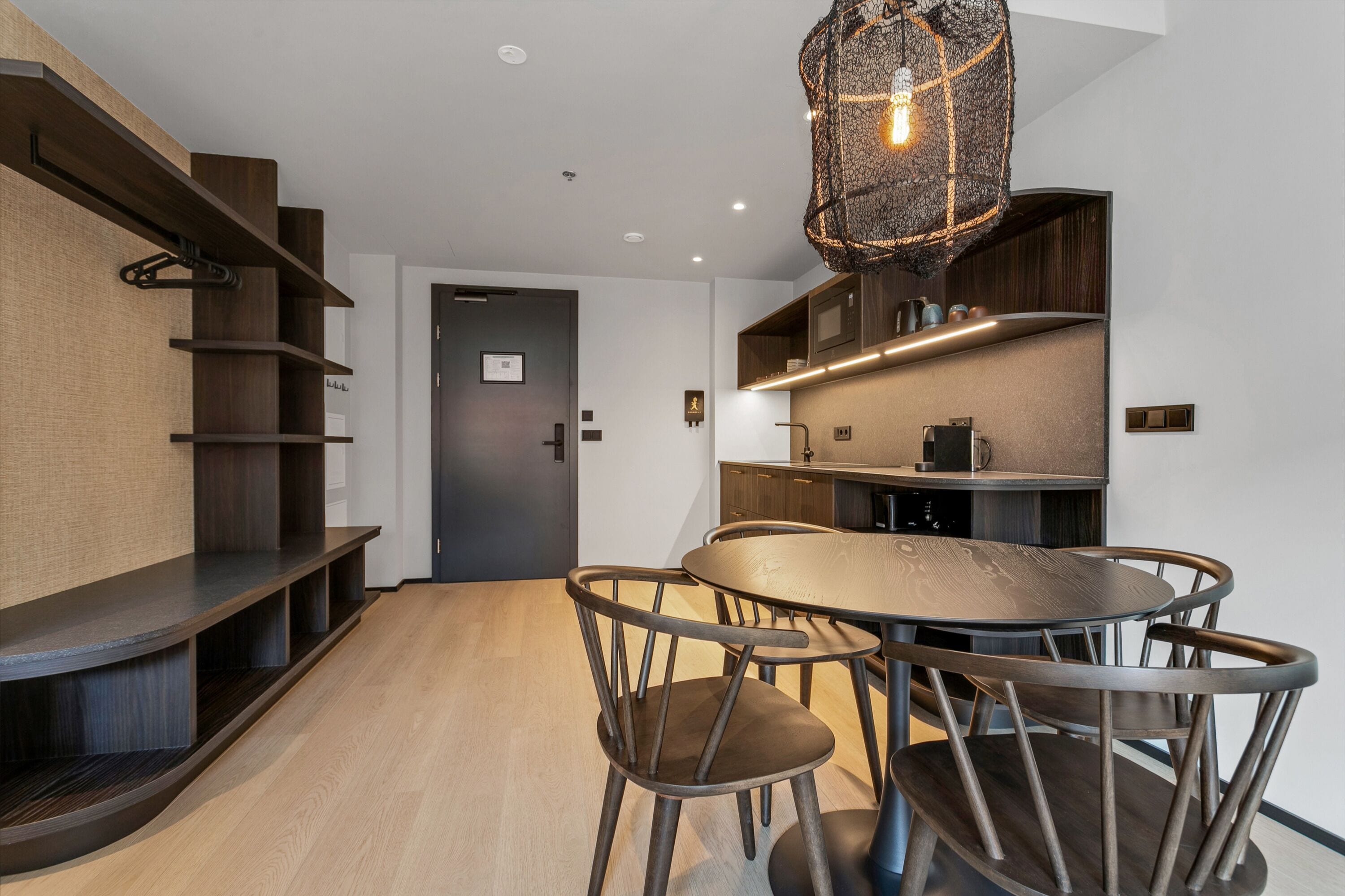 Une cuisine moderne avec une table à manger ronde et des chaises, des étagères en bois et un luminaire suspendu.