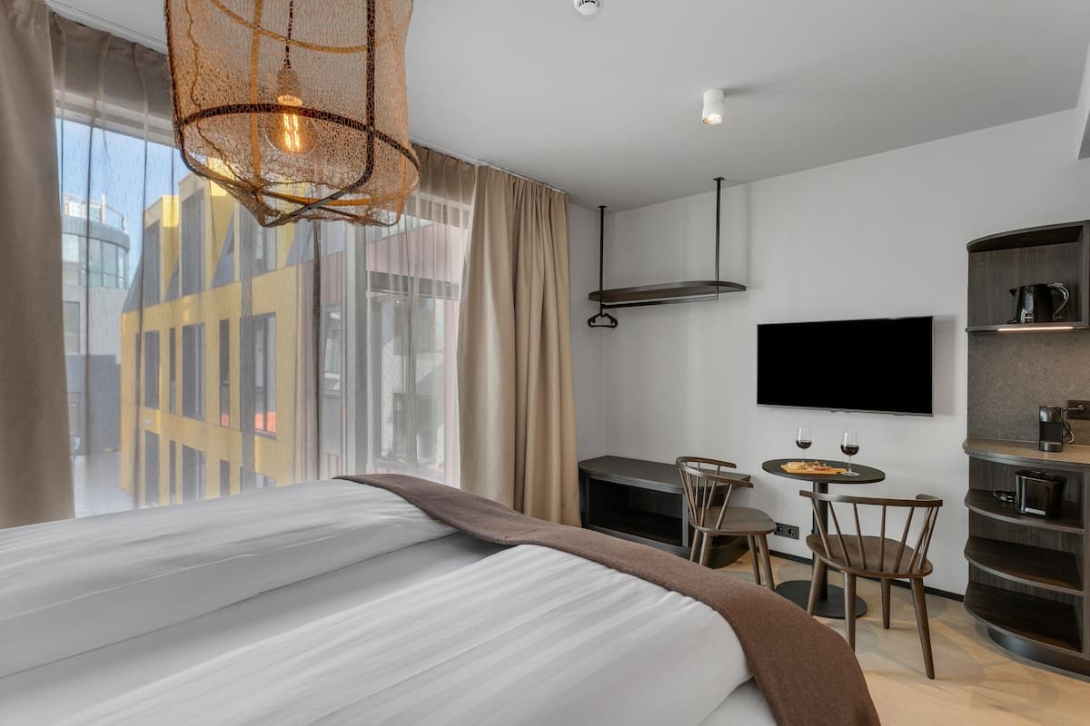 A modern hotel room with a large bed, a desk with a chair, a television, and a coffee machine.