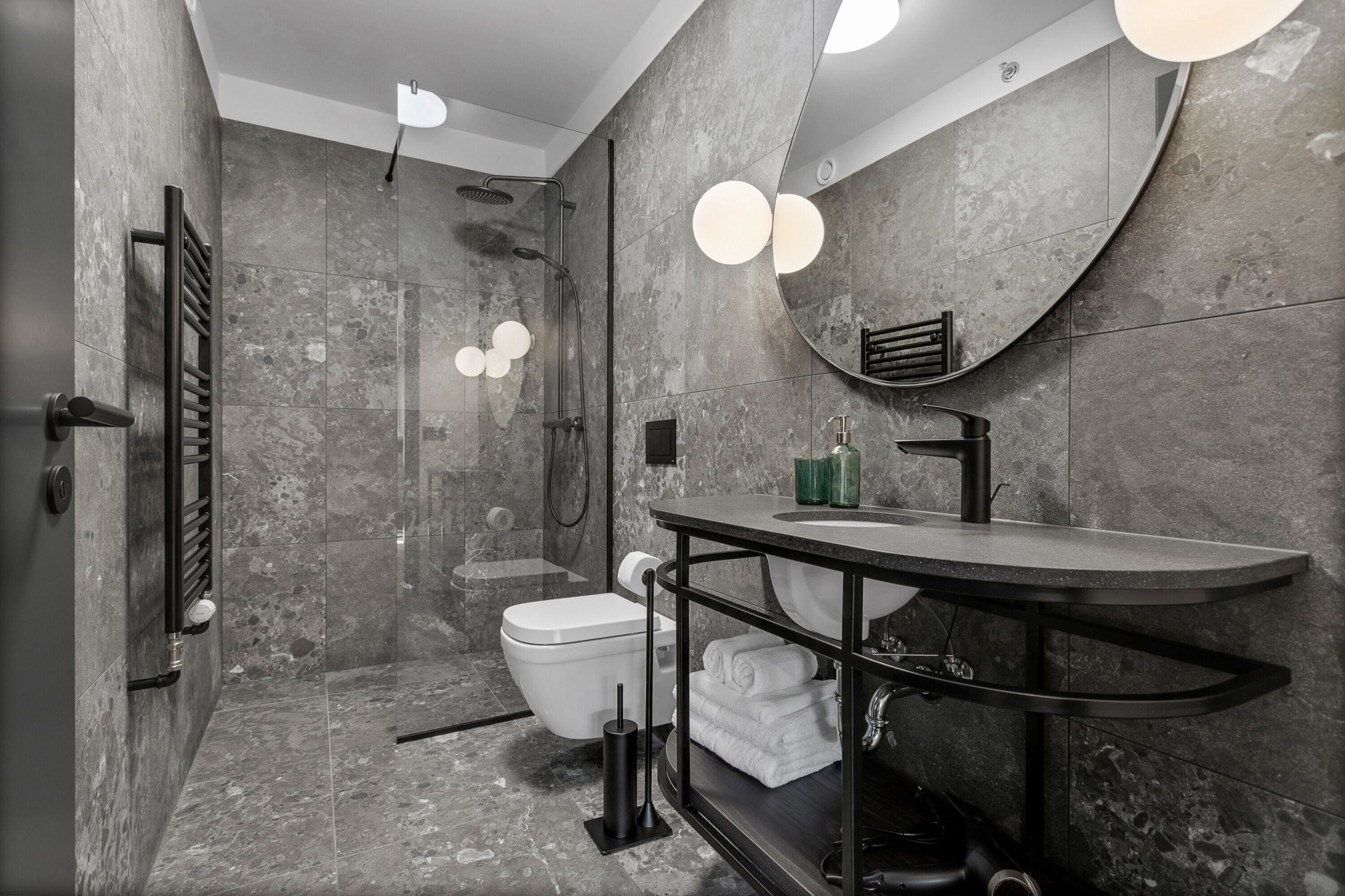 A modern bathroom with a curved sink, a glass shower enclosure, and a marble-tiled wall.