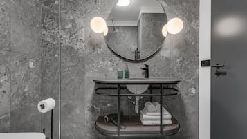 Un baño con pared de mármol, un espejo redondo con luces, un lavabo con toallero y un inodoro.