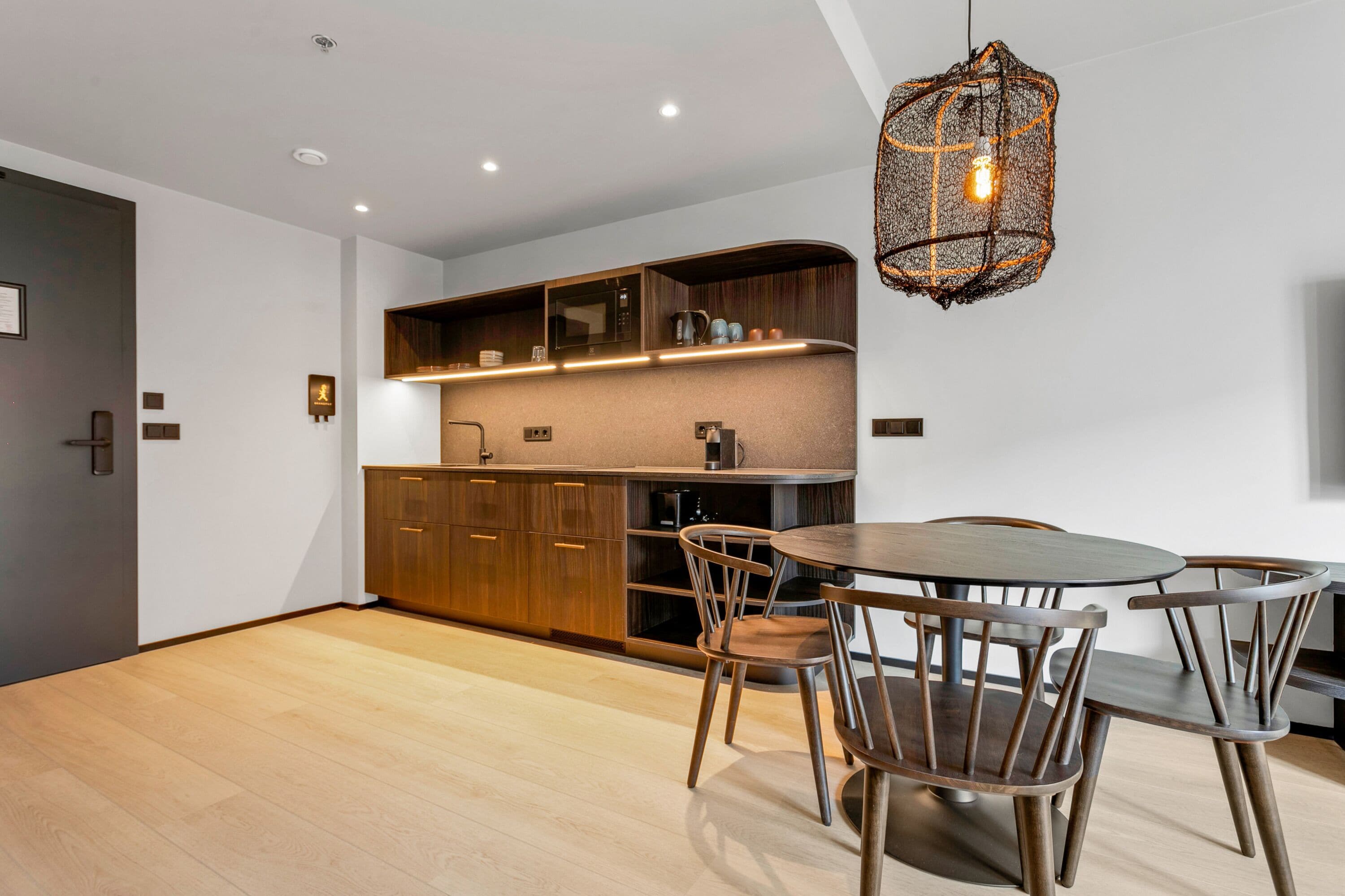 Een moderne keuken met houten kasten, een inbouwoven en een eethoek met een ronde tafel en stoelen.