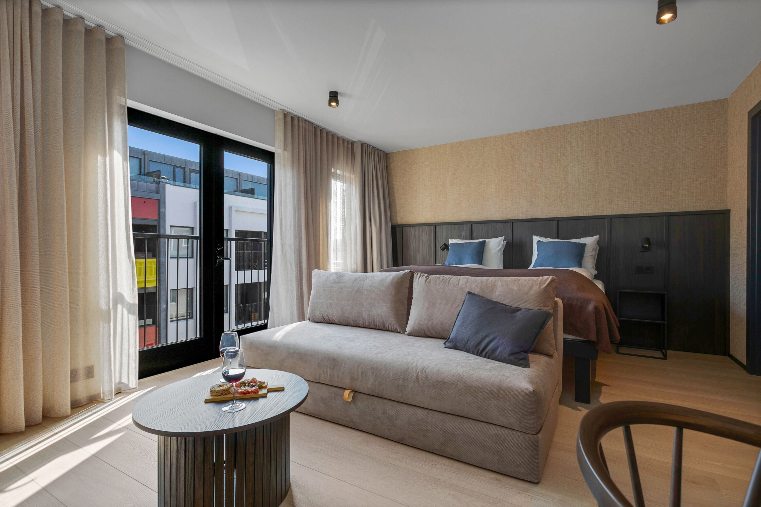 Una habitación de hotel moderna con un sofá, una mesa redonda pequeña y una cama con cabecera.
