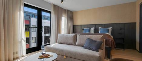 Una habitación de hotel moderna con un sofá, una mesa redonda pequeña y una cama con cabecera.