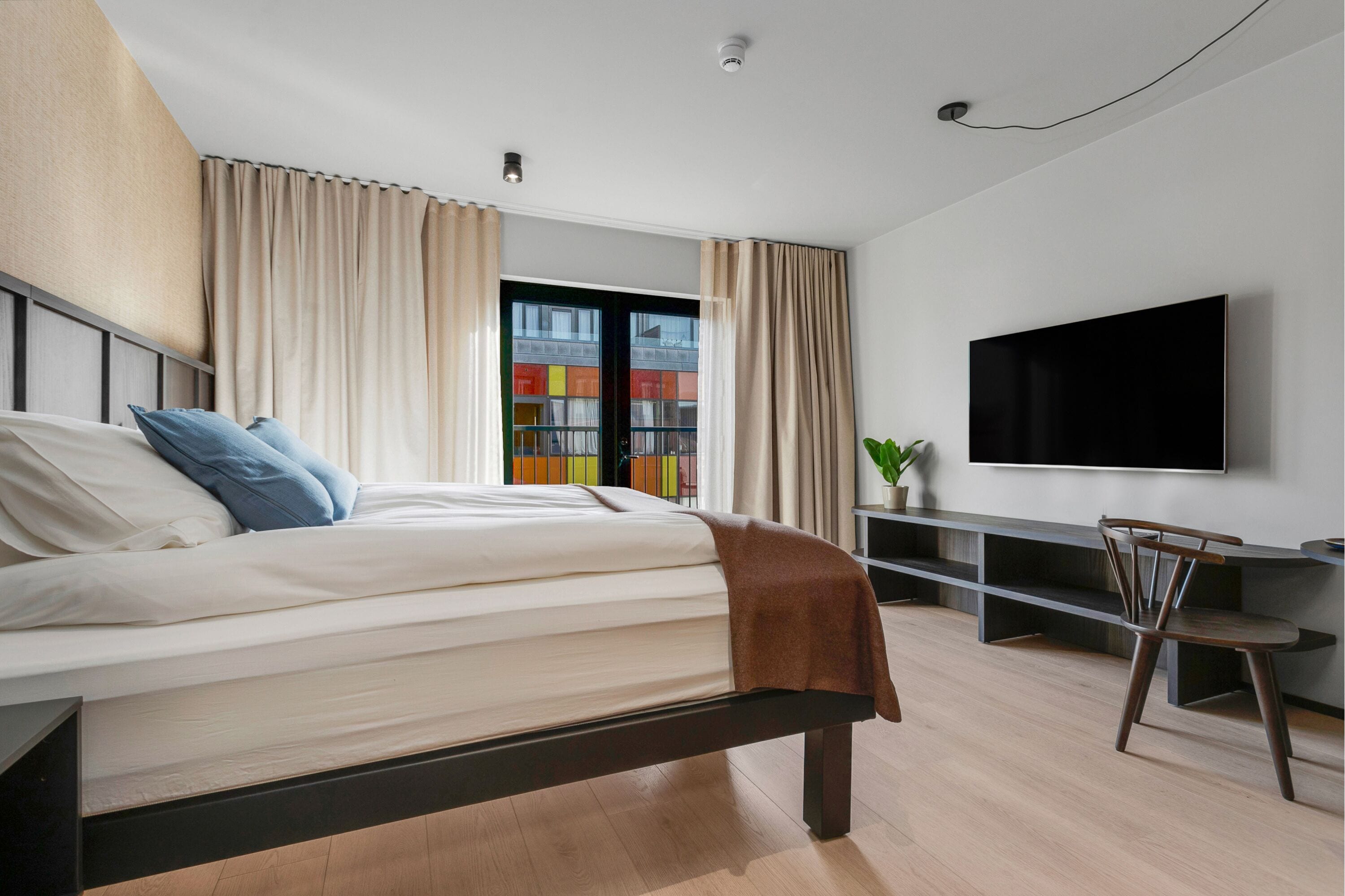 A modern bedroom with a bed, curtains, a TV, a desk, and a chair.