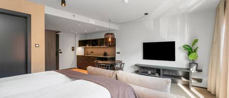 A modern hotel room with a large bed, a dining area, and a TV mounted on the wall.