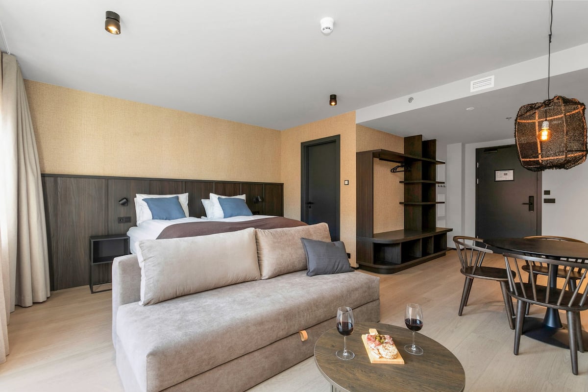 A modern hotel room with a bed, sofa, dining table, and chairs.