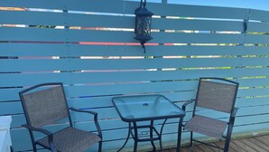A patio with two metal chairs and a small table, a blue fence, and a lantern. - Casita Heliconia- Jr. Suite#3 (Roseau)