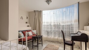 Un salon chaleureux avec un canapé, un piano et une vue sur la ville, visible à travers de fines rideaux.