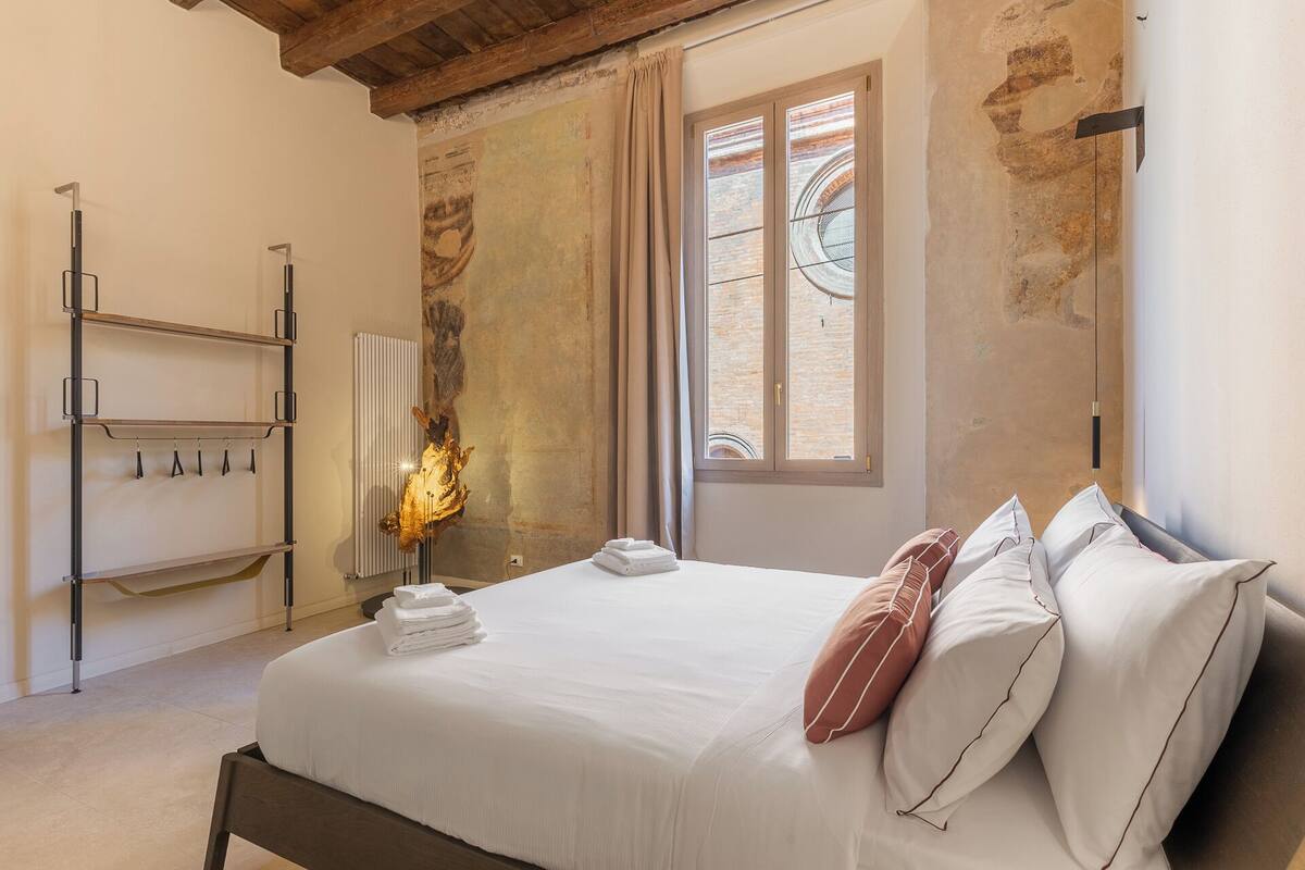 A bedroom with a bed, a radiator, a window with curtains, and a wall-mounted shelf.