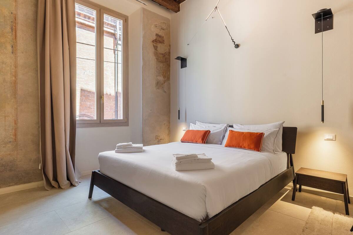 A bedroom with a bed, a bedside table, a lamp, and a window with curtains.