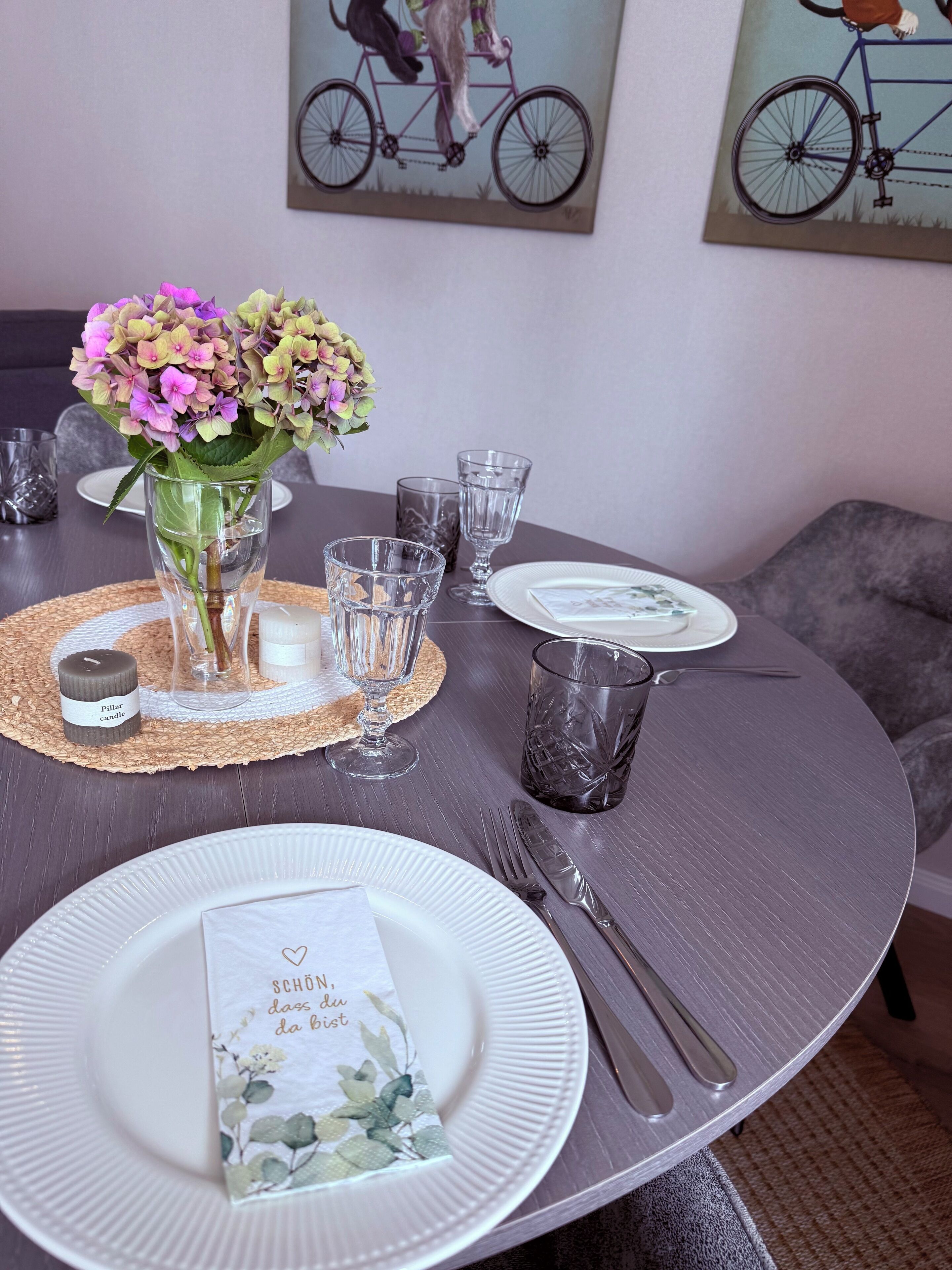 A dining table set with plates, cutlery, glasses, a candle, and a vase with flowers.