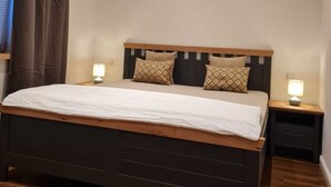 A bedroom with a wooden bed, two bedside tables, and recessed ceiling lights. - Ida vacation apartment - your temporary home in the Harz Mountains. (Quedlinburg)